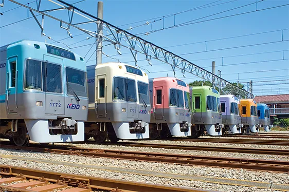 レインボー車両がブルーグリーン、アイボリーホワイト、サーモンピンク、ライトグリーン、バイオレット、オレンジベージュ、ライトブルーと順に並んでいる写真